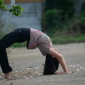 Girl doing Chakrasana on road with fall leaves